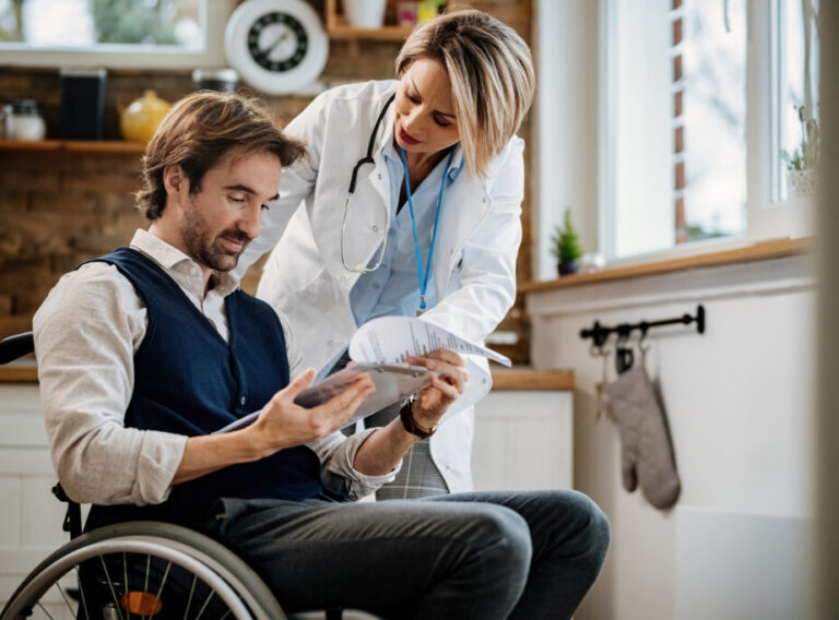 Young smiling man in wheelchair and his doctor analyzing medical reports during home visit.